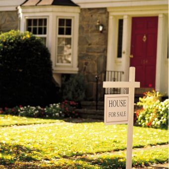 Board in front of a house displaying 'for sale advertisement'.